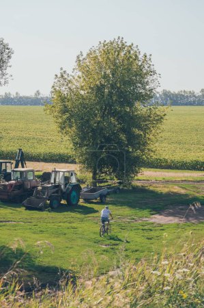 Photo for Woman rides bicycle past machinery to sunflower field - Royalty Free Image