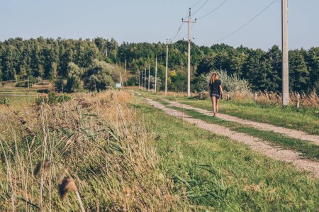 Photo for Row of electric poles with wires, woman walks down country road - Royalty Free Image