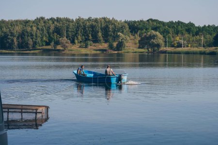Foto de Dos pescadores en lancha a motor navegan en el río contra la vista del bosque - Imagen libre de derechos