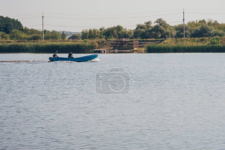 Foto de Dos pescadores en lancha a motor navega en el río, observador en la orilla alta - Imagen libre de derechos