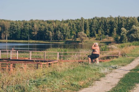 Téléchargez les photos : Vieux gardien assis sur la rive haute contre le paysage forestier - en image libre de droit