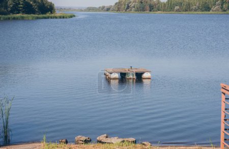 Photo for Summer sunny river landscape, wooden pier on barrels on blue water - Royalty Free Image