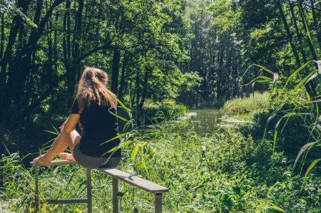 Téléchargez les photos : Femme assise et profitant du soleil et du paysage forestier - en image libre de droit