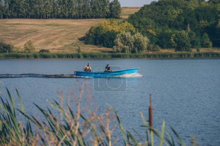 Photo for Two fishemen in motor boat sails dissecting waves on river water - Royalty Free Image
