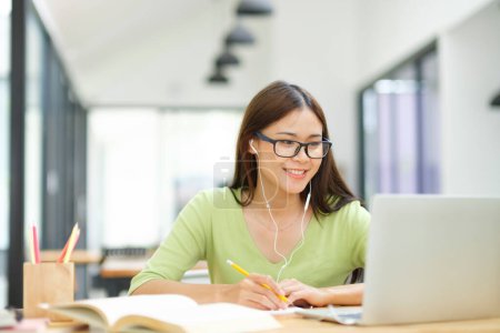 Téléchargez les photos : Jeune étudiante asiatique étudier à la maison en utilisant un ordinateur portable et l'apprentissage en ligne. Entreprise freelance vidéoconférence par ordinateur portable à la maison. - en image libre de droit