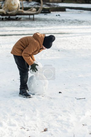 Photo for Boy puts snow balls on top of each other. - Royalty Free Image