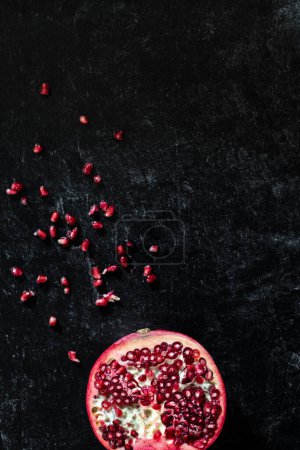 Minimal Pomegranate Slice and seeds on dark black tabletop