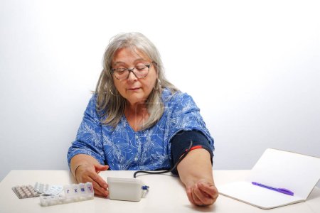 Photo for Older white-haired woman taking her blood pressure at home - Royalty Free Image