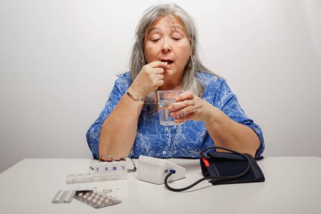 Téléchargez les photos : Femme prenant une pilule après avoir fait vérifier sa tension artérielle - en image libre de droit