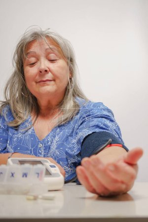 Foto de Mujer mayor de pelo blanco tomando su presión arterial en casa - Imagen libre de derechos