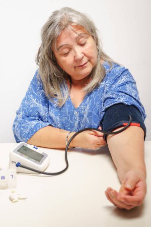Foto de Mujer mayor de pelo blanco tomando su presión arterial en casa - Imagen libre de derechos