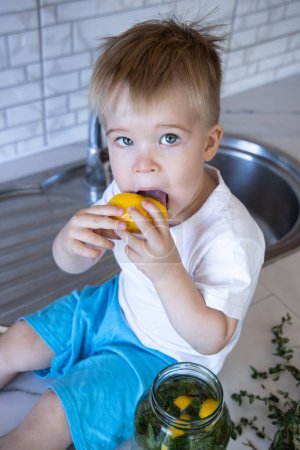 Téléchargez les photos : Petit garçon lèche un citron assis sur une table - en image libre de droit