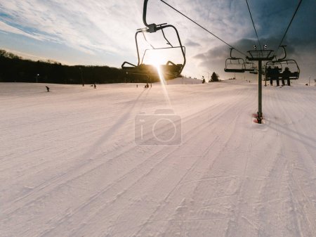 Photo for Sun sets over ski lift with people coming down hill in distance - Royalty Free Image