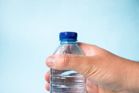 Téléchargez les photos : Prendre à la main bouteille d'eau en plastique sur fond bleu - en image libre de droit