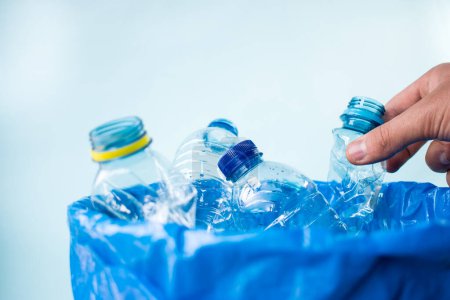 Téléchargez les photos : Homme laissant une bouteille en plastique dans un bac de recyclage bleu - en image libre de droit
