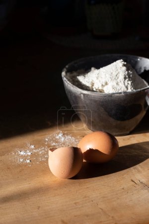 Téléchargez les photos : Ingrédients pour faire de la pâte - farine dans un bol, œufs. Lumière dure - en image libre de droit