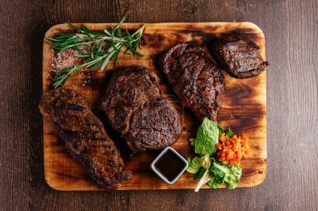 Téléchargez les photos : Quatre types de steaks différents sur une planche de bois - en image libre de droit