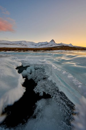 Téléchargez les photos : Vue pittoresque de la glace fendue révélant l'eau calme de la rivière en hiver au coucher du soleil - en image libre de droit