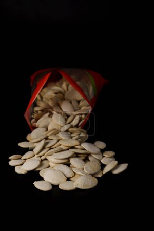 Photo for Roasted pumpkin seeds with salt coming out of their red bag on a black table with copy space - Royalty Free Image