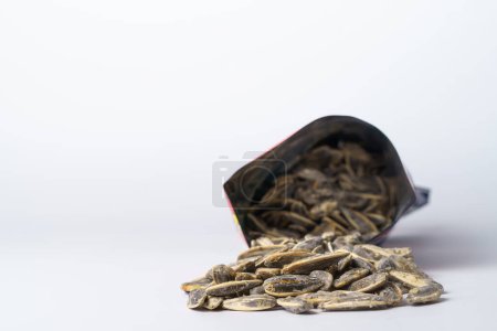 Photo for Roasted sunflower seeds with salt coming out of their bag on white background and copy space - Royalty Free Image