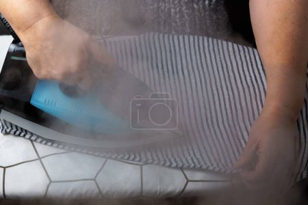 Photo for Woman ironing a striped T-shirt while steaming - Royalty Free Image