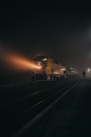 Photo for Passenger train arriving at a quiet railway station on a foggy night. - Royalty Free Image
