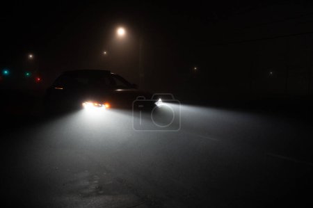 Photo for Car driving down a deserted street on a foggy autumn night. - Royalty Free Image