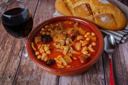 Foto de Cazuela de barro con callos guisados de estilo madrileño, comida típica española sobre una mesa de madera con una pared de ladrillo en el fondo. - Imagen libre de derechos