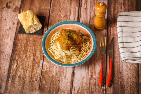 Foto de Plato de albóndigas con espaguetis con cubiertos y batidora de pan y pimienta sobre una mesa de madera - Imagen libre de derechos