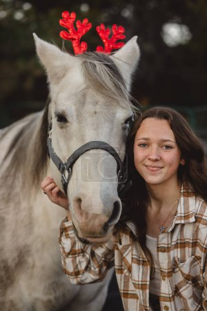 Téléchargez les photos : Oreilles de renne sur un cheval blanc avec jeune fille - en image libre de droit