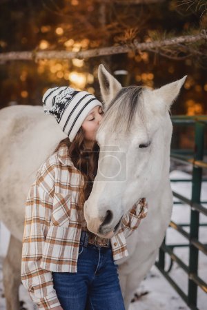 Téléchargez les photos : Adolescent fille baisers blanc cheval dans coucher de soleil - en image libre de droit