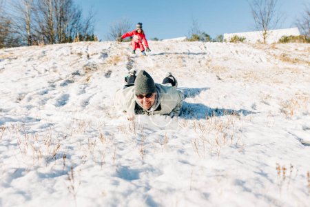 Photo for Father and daughter sliding down a snowy hill - Royalty Free Image