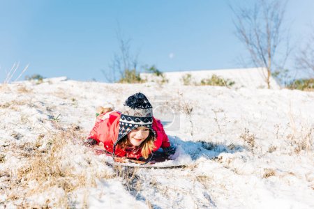 Foto de Young girl sliding down snowy hill against blue sky with moon - Imagen libre de derechos