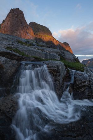 Foto de Pequeña cascada fluye por debajo del pico de montaña Litlklokktind, parque nacional Lofotodden, Moskenesy, Islas Lofoten, Noruega - Imagen libre de derechos