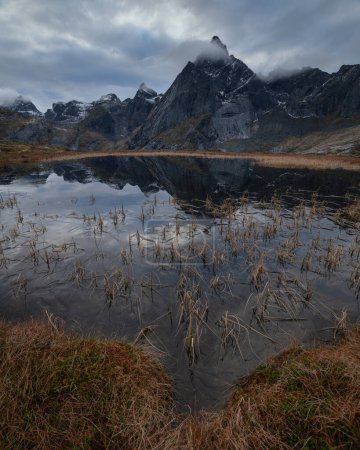 Photo for Stortind mountain peak reflects in frozen autumn pond, Flakstady, Lofoten Islands, Norway - Royalty Free Image