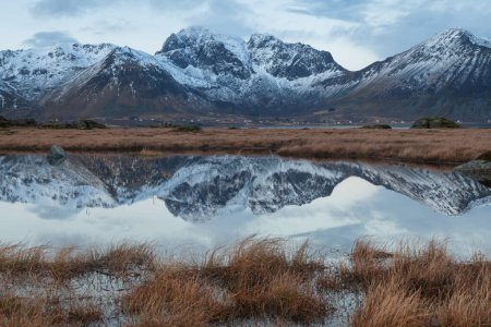 Photo for Snow covered mountain peaks reflect in small pond, Vestvgy, Lofoten Islands, Norway - Royalty Free Image