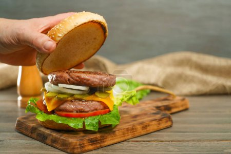 Téléchargez les photos : Gros plan des mains d'une femme ouvrant le pain d'un pain de hamburger avec deux morceaux de viande sur une planche en bois - en image libre de droit