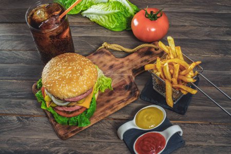 Téléchargez les photos : Hamburger complet avec deux viandes, sauces, frites et cola sur une planche de bois antique. - en image libre de droit