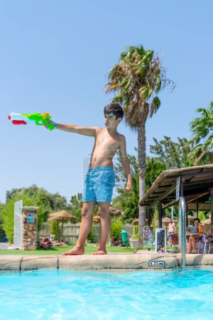 Foto de Niño moreno jugando con la pistola de agua en la piscina de un camping en un país tropical - Imagen libre de derechos