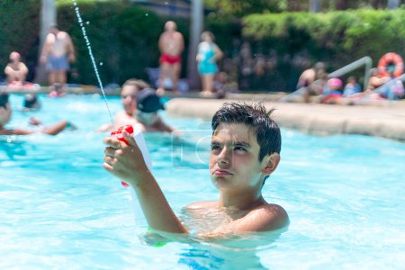 Photo for Dark-haired boy playing with the water gun in the pool of a campsite in a tropical country - Royalty Free Image