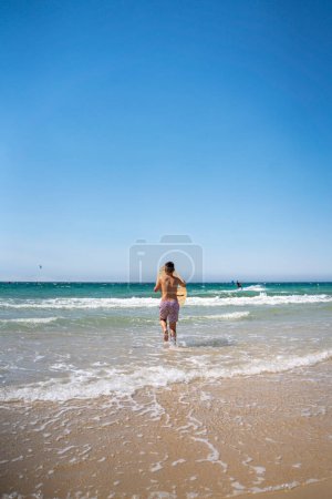Photo for Dark-haired boy surfing with his skinboard on a beach in southern Spain - Royalty Free Image
