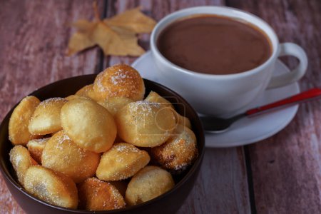 Téléchargez les photos : Beignets faits maison avec sucre dans un bol et chocolat chaud dans une tasse blanche sur une table en bois - en image libre de droit
