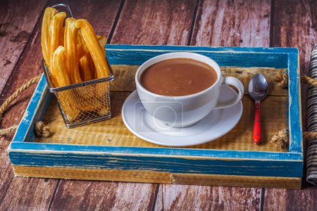 Téléchargez les photos : Chocolat chaud dans une tasse blanche avec des churros dans un plateau en bois bleu sur une table en bois - en image libre de droit