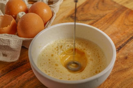 Photo for Beating an egg in a bowl with a small mixer with an egg cup at the bottom on a wooden table - Royalty Free Image