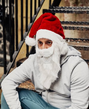Téléchargez les photos : Père Noël sans abri buvant du vin et fouillant dans les poubelles - en image libre de droit