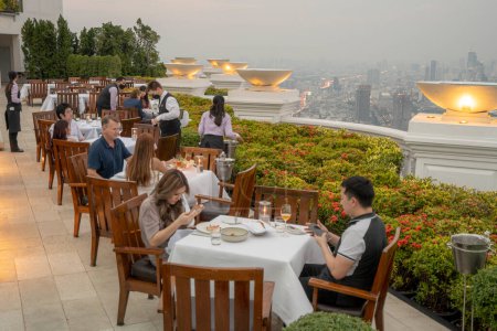 Foto de Tourists Enjoying Luxurious Dinner At A Rooftop Sky Bar at Sunset - Imagen libre de derechos