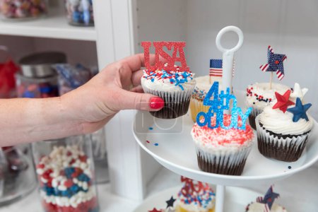 Photo for Female hand takes Fourth of July themed cupcakes off display plate - Royalty Free Image