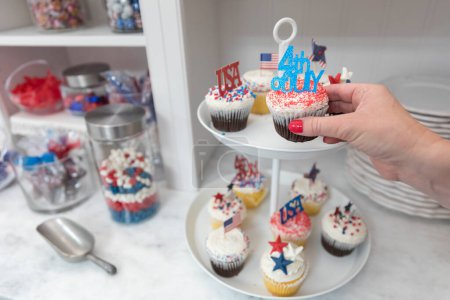 Photo for Female hand takes Fourth of July themed cupcakes off display plate - Royalty Free Image