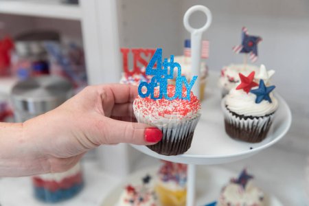 Photo for Female hand taking Fourth of July themed cupcakes off display plate - Royalty Free Image
