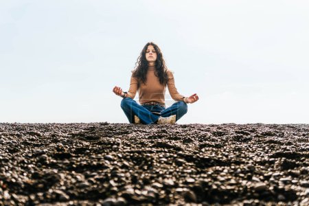 Photo for Woman sitting meditating on black stone beach in positano - Royalty Free Image